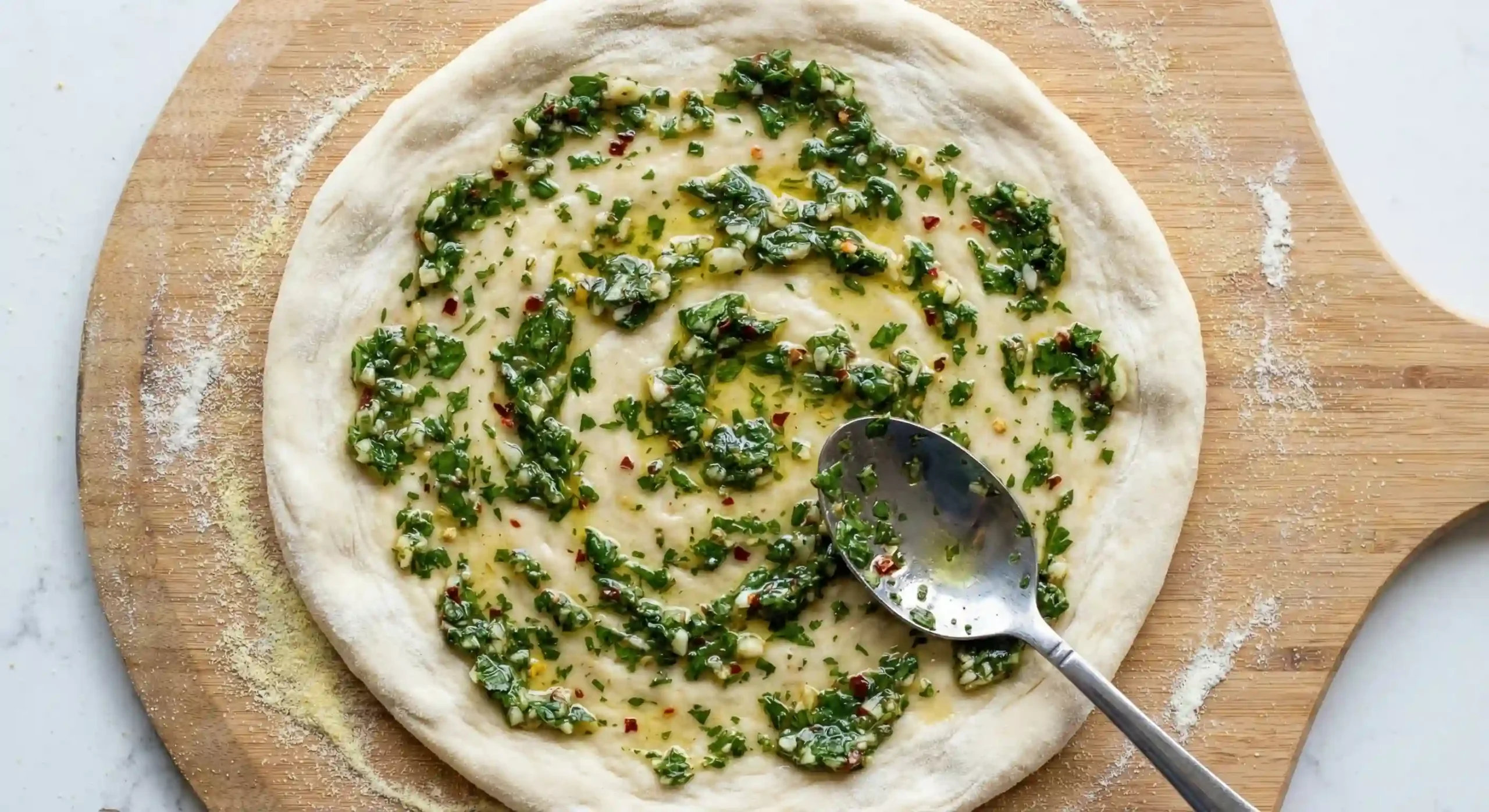 Thin layer of chimichurri spread on pizza dough as the base