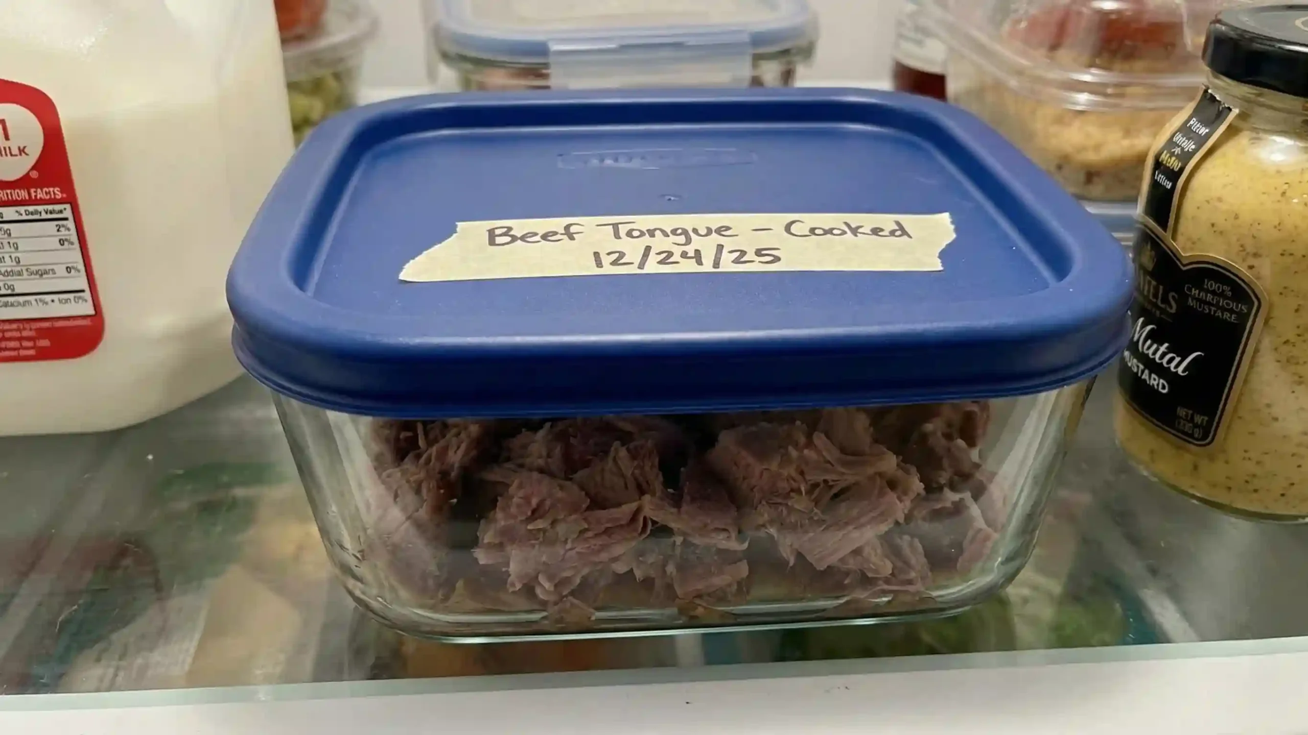 A labeled airtight container inside a refrigerator storing cooked beef tongue leftovers with the date clearly written on masking tape