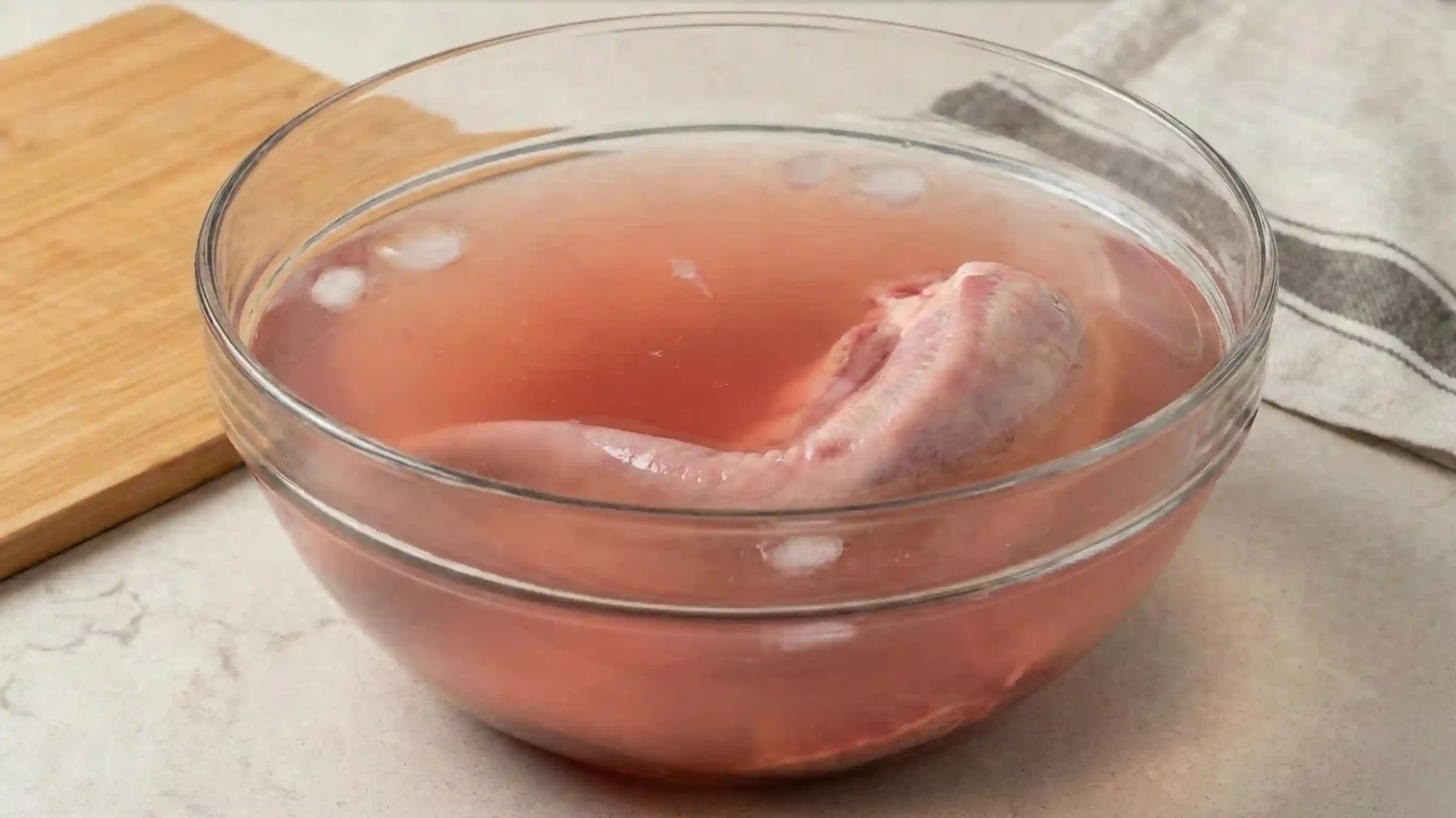 Raw beef tongue submerged in a bowl of cold water turning pink to illustrate the soaking and cleaning process